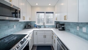 Una cocina moderna con armarios blancos, una estufa de acero inoxidable y una ventana sobre el fregadero.