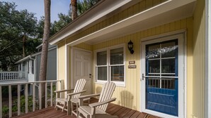 Una terraza de madera con sillas Adirondack, una puerta azul y un cartel que dice '528 FLOOD'.