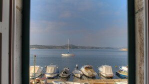 Une vue sur un port où plusieurs bateaux sont amarrés, un voilier à l’horizon et un paysage vallonné de l’autre côté de l’eau.