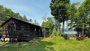 A rustic cabin with a porch, surrounded by lush greenery and a lake view. - Lake Front Cabin with free WiFi - Adirondacks High Peaks Region - Lake Placid (Elizabethtown)