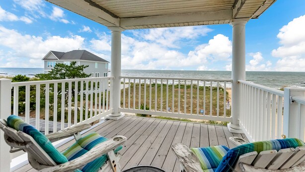 A wooden deck with two lounge chairs and a small table, overlooking a beach and ocean. - 3-Story Oceanfront • Breathtaking Views • Dogs OK (Norfolk)
