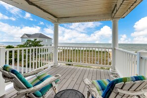 A wooden deck with two lounge chairs and a small table, overlooking a beach and ocean.