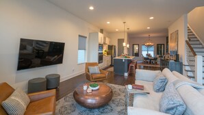 Un salon spacieux avec un grand téléviseur à écran plat, un fauteuil en cuir marron, une table basse ronde et un canapé blanc.