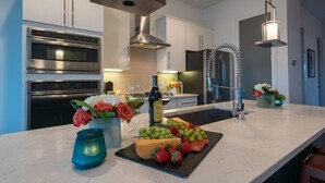 Une cuisine moderne dotée d’appareils électroménagers intégrés, d’un plan de travail en marbre et d’un îlot central où sont présentés des fruits et des fromages.