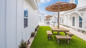 Un bâtiment blanc doté d’un patio couvert, d’une pelouse verdoyante et de tables de pique-nique en bois.