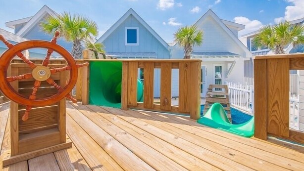 Une terrasse en bois avec une roue de navire, un toboggan et une piscine.