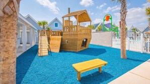 Un espace de jeux pour enfants avec une cabane en bois, un toboggan et un banc.