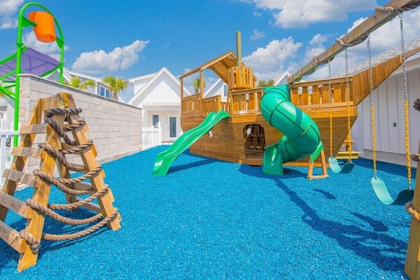 Un parque infantil con un tobogán de madera, una estructura para escalar con cuerdas y una zona de juegos con temática náutica.