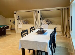 Een gezellige kamer met een eettafel, stoelen, een pooltafel en twee stapelbedden met gordijnen.