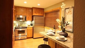 A kitchen with wooden cabinets, stainless steel appliances, a granite countertop, and a dining area with a vase of flowers. - Modern Hotel-Like Luxury! 3 Bed+Loft. Twin Units  Book Separately 329292 (Mammoth Lakes)