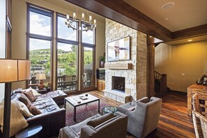 Un salón amplio con chimenea de piedra, ventanas grandes que ofrecen vistas al exterior y un rincón de estar acogedor.