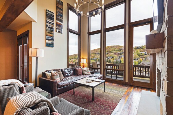 Ein geräumiges Wohnzimmer mit großem Fenster, einer Ledersofa, einem Couchtisch und Blick auf eine hügelige Landschaft.