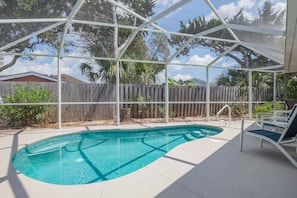 A covered outdoor swimming pool with a wooden fence and lounge chairs. - Robin's Nest: Private 4 bedroom Pool home just steps to beach with screen pool (St. Augustine Beach)