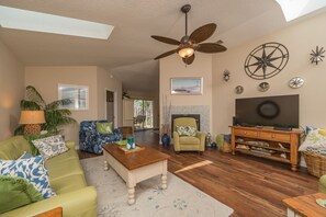 A spacious living room with a ceiling fan, a fireplace, a television, and a dining area. - Robin's Nest: Private 4 bedroom Pool home just steps to beach with screen pool (St. Augustine Beach)
