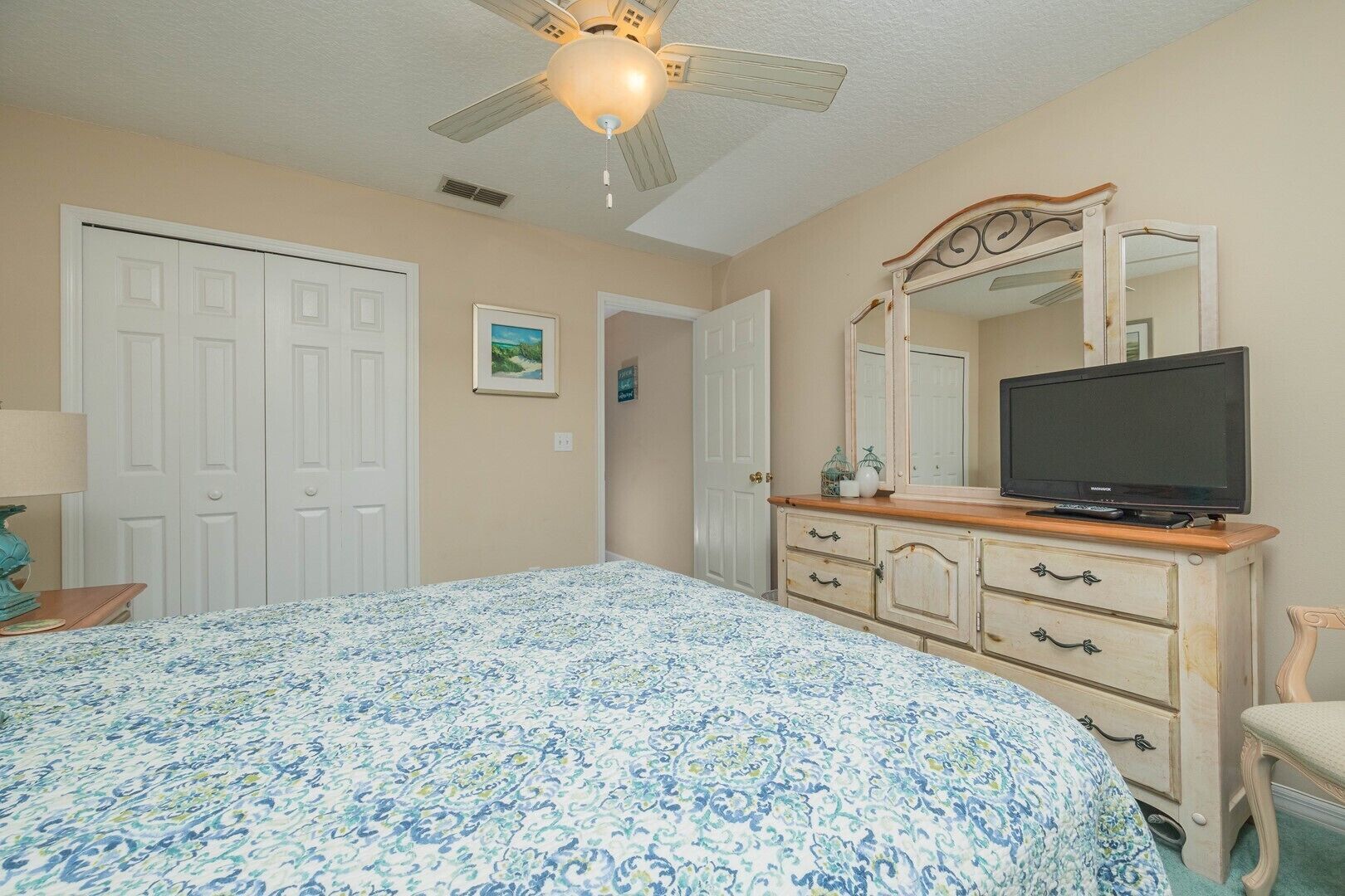 A bedroom with a bed, dresser, television, and ceiling fan.