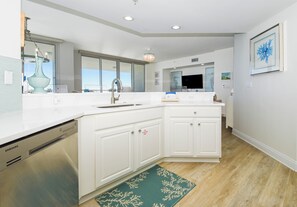 A modern kitchen with white cabinetry, a stainless steel dishwasher, a large island with a sink, and a green decorative rug.