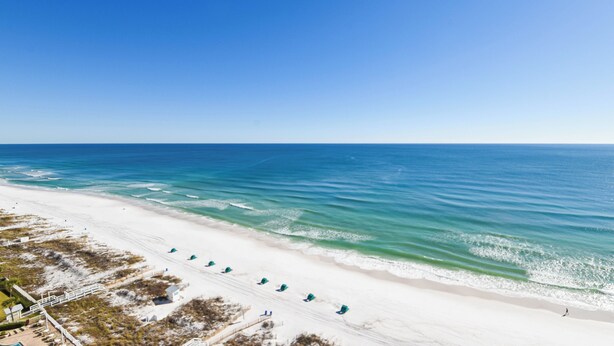 Ein Strand mit weißem Sand, klarem, blauem Wasser und einigen Strandliegen.