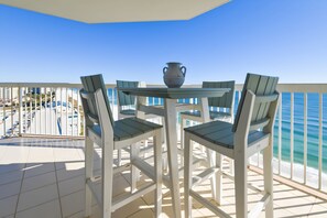 A balcony with a table and chairs, overlooking a beach.