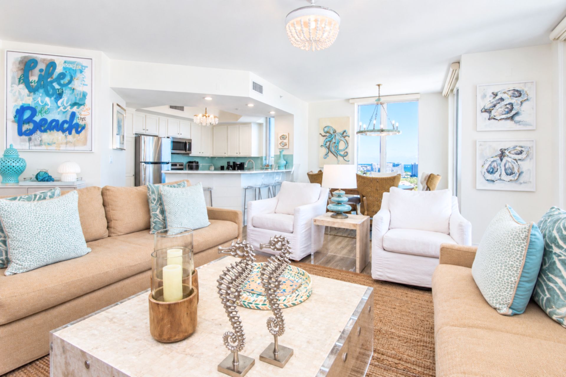 Una sala de estar moderna con un sofá color beige, sillones blancos, una mesa de centro con objetos decorativos y una cocina al fondo.
