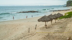 Een strand met rieten parasols, een zandstrand en uitzicht op de oceaan.