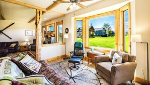 A spacious living room with a large window, a ceiling fan, and a view of a green landscape. - Golf Course Mountain Home , Views/Hot Tub/Star Gazing/Ski/Hike/Golf/Gather/Relax (Red Lodge)