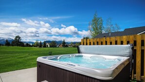 A hot tub with a wooden deck and a view of a grassy yard and mountains. - Golf Course Mountain Home , Views/Hot Tub/Star Gazing/Ski/Hike/Golf/Gather/Relax (Red Lodge)
