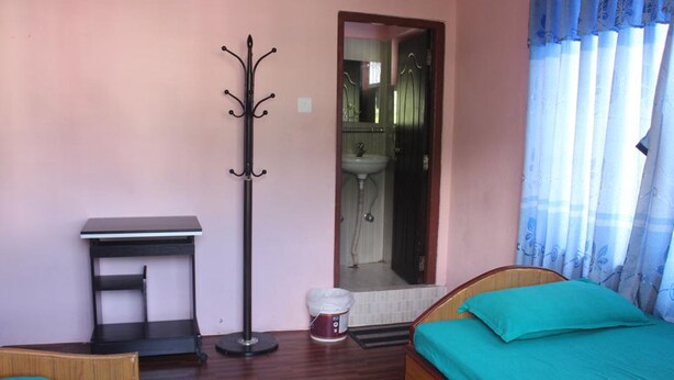 A bedroom with a bed, a desk, a coat rack, and a bathroom visible through an open door. - Goldenbirds Homestay (Pokhara)