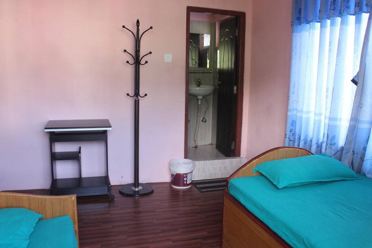 A bedroom with a bed, a desk, a coat rack, and a bathroom visible through an open door.