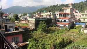 A residential area with multi-story buildings, some with balconies, surrounded by greenery and hills in the background. - Goldenbirds Homestay (Pokhara)