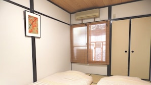 A small, single-room with two beds, a window with a view, and a wall-mounted air conditioner. - Guest House Motana (Kyoto)
