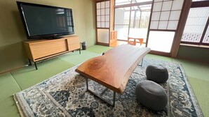 A traditional Japanese room with tatami flooring, a low wooden table, a television on a wooden stand, and a sliding shoji screen door.