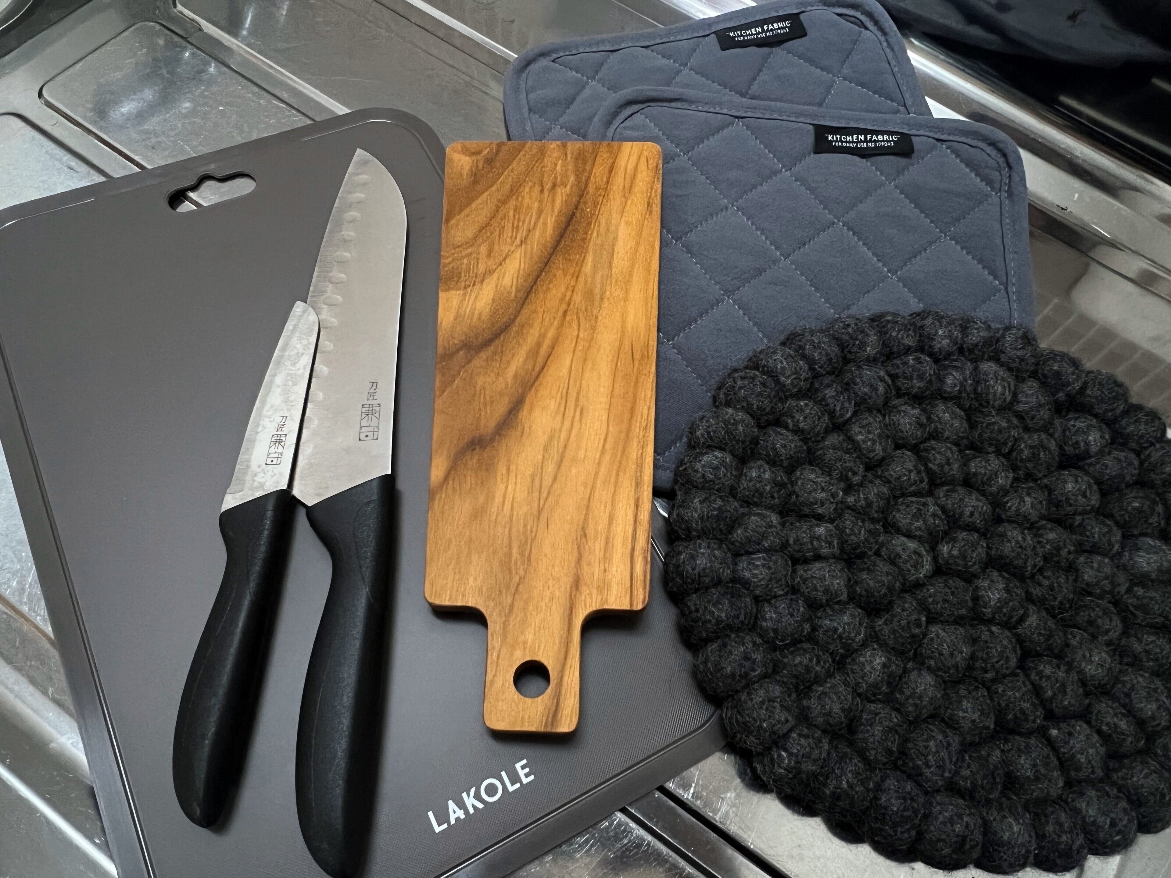 A kitchen knife, a wooden cutting board, and a black kitchen mat on a black cutting board labeled "LAKOLE".
