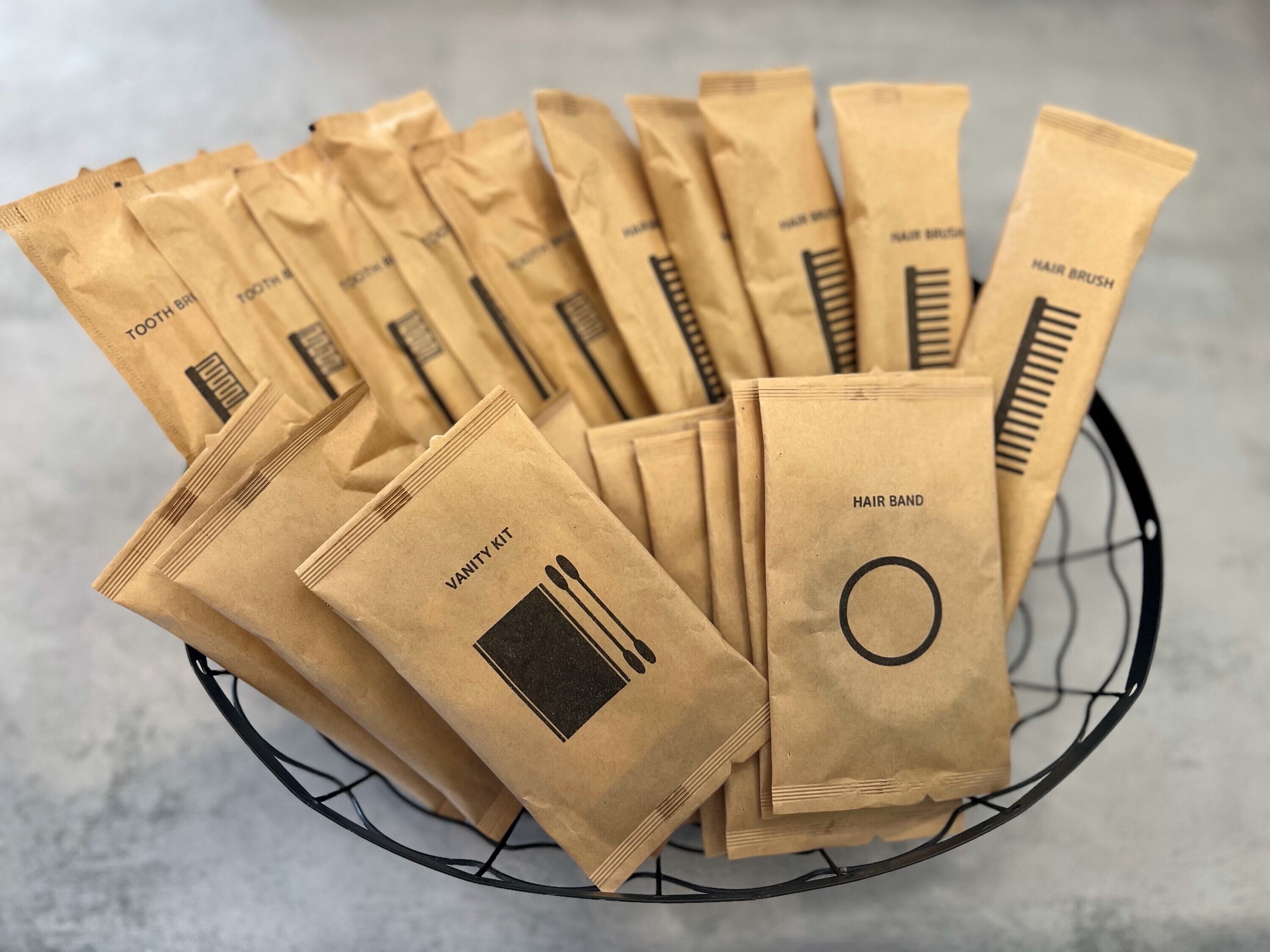 A basket filled with brown paper bags labeled with various hair care items like toothbrushes, hairbrushes, and hairbands.