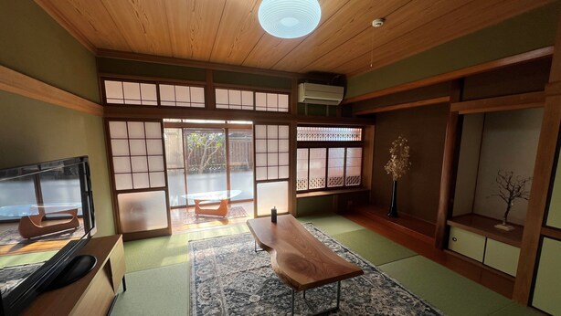 A traditional Japanese-style room with tatami flooring, a low wooden table, a television, and sliding doors leading to an outdoor area.