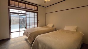 A room with two beds, a sliding glass door leading to a balcony, and a ceiling light fixture.