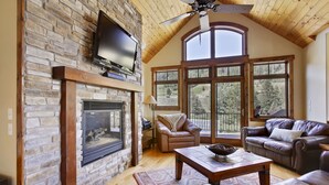A spacious living room with a stone fireplace, leather sofas, and large windows offering a view of the outdoors.