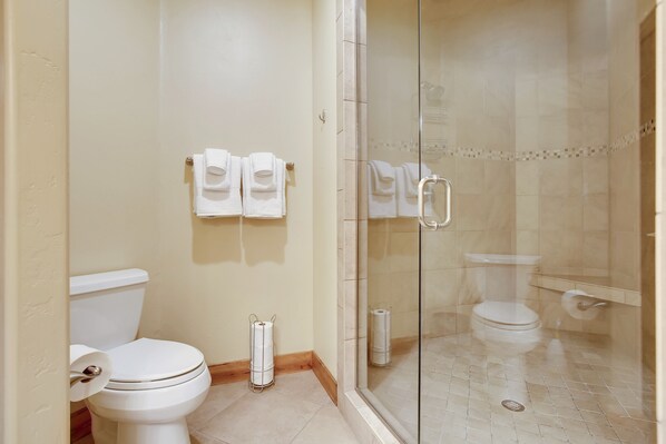 Un baño con inodoro, ducha con cerramiento de vidrio y dos toallas colgadas en la pared.