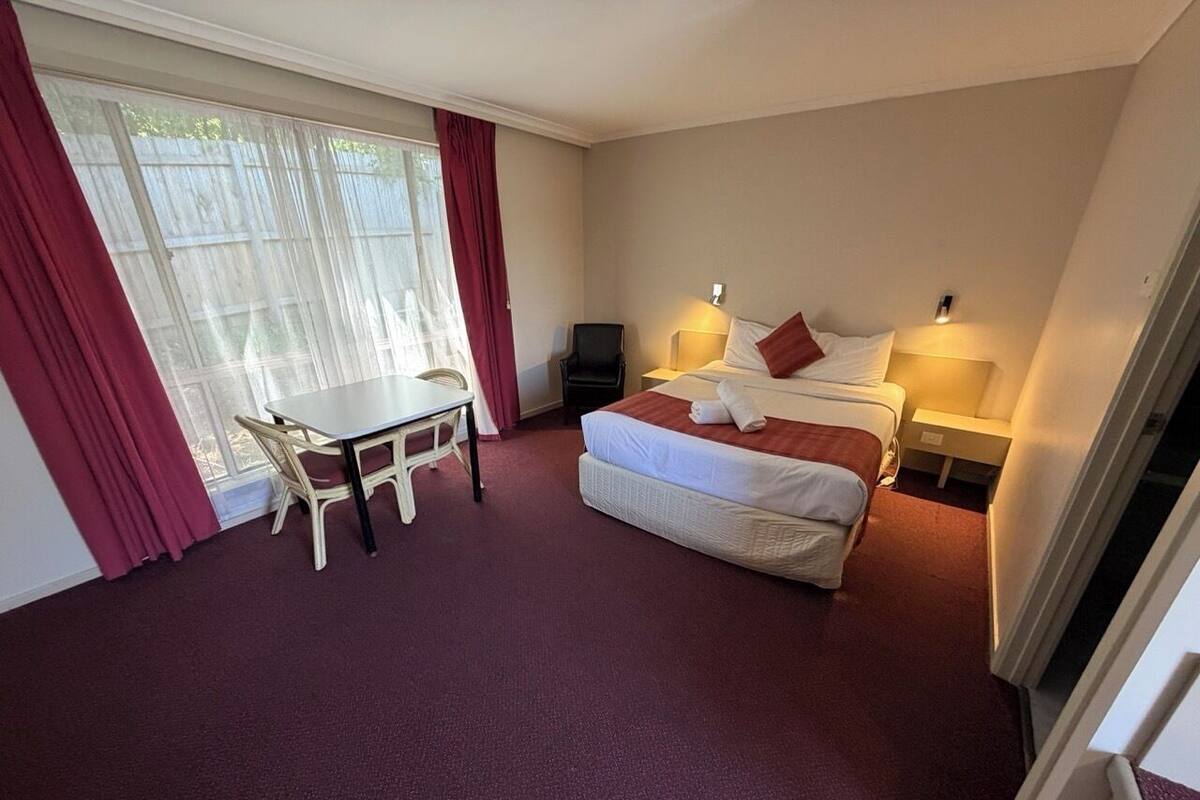 A hotel room with a bed, bedside tables, a chair, a small table, and a window with curtains.