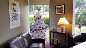 Uma sala de estar com uma árvore de Natal branca, um sofá de couro marrom, uma mesinha com um abajur e um quadro emoldurado na parede.
