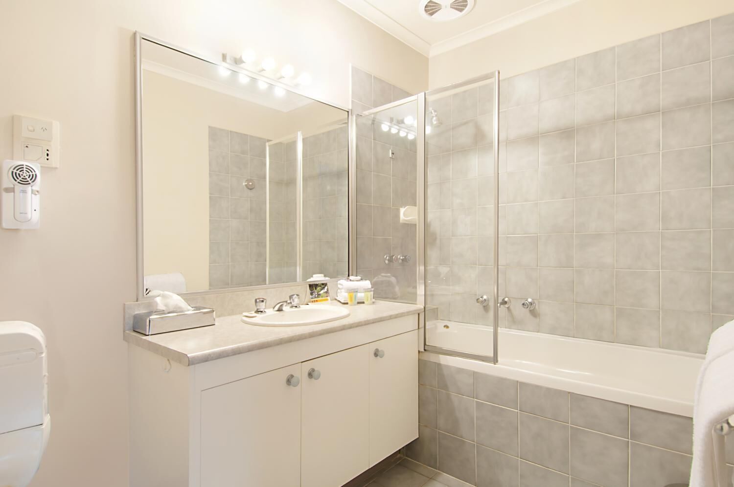 A modern bathroom with a large mirror, a sink with toiletries, a shower enclosure, and a toilet.