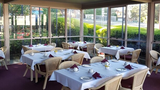 Um restaurante com mesas preparadas para refeições, grandes janelas e vista para o exterior.