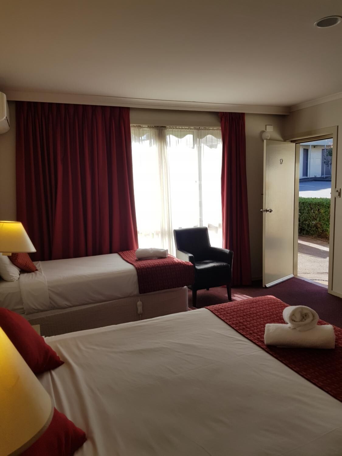A hotel room with two beds, a chair, a desk, and a door leading outside.