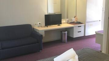 Una habitación de hotel con cama, escritorio, televisor, armario y cesto de basura.