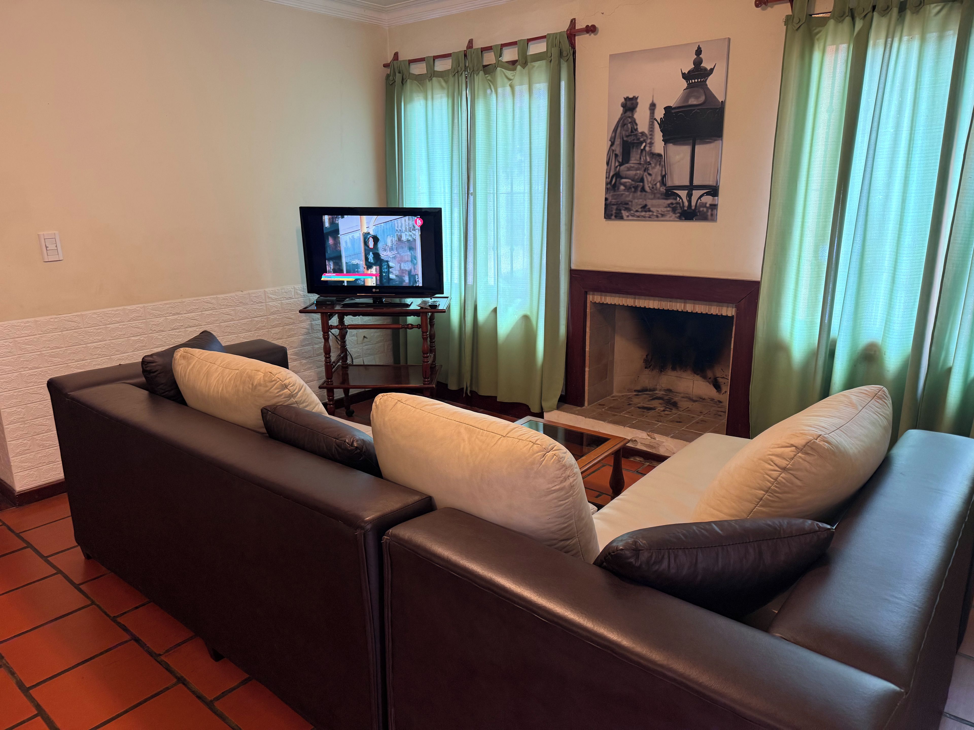 Un salón con un juego de sofá, televisor, chimenea y cortinas verdes.