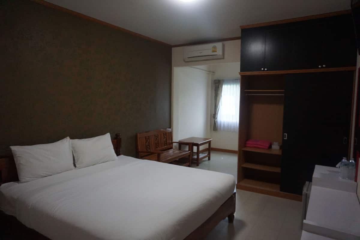 A bedroom with a bed, a wooden nightstand, a desk, a chair, and a wardrobe.