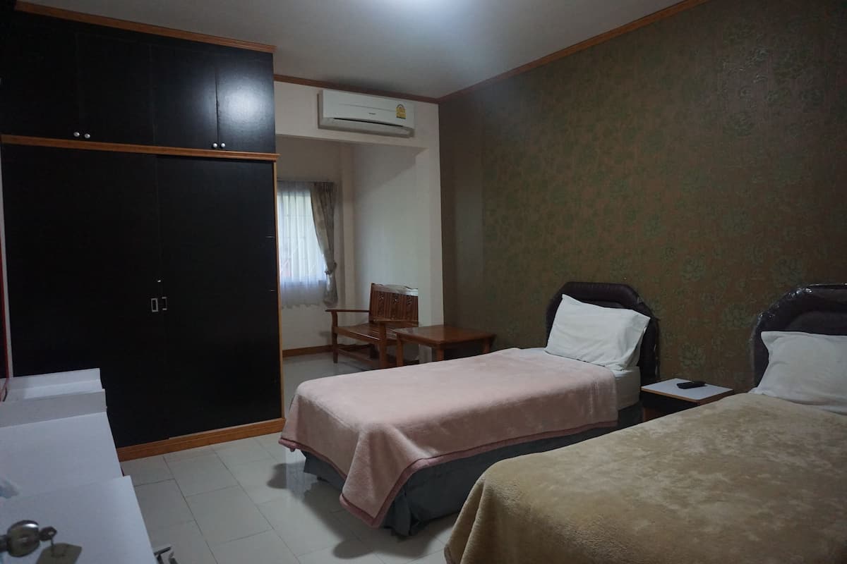 A hotel room with a wardrobe, two beds, a desk, a chair, and an air conditioning unit.