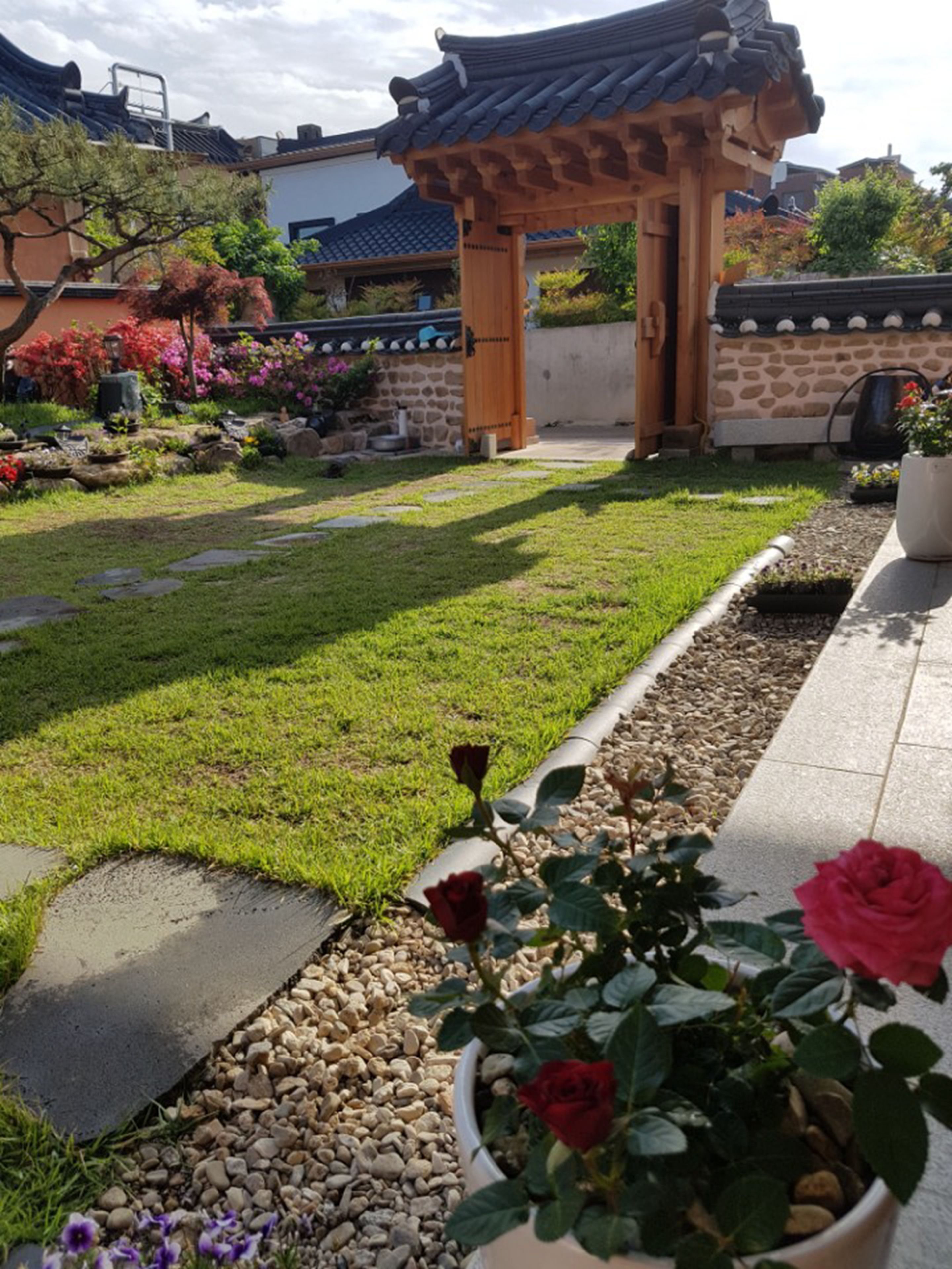 Un jardín japonés tradicional con un sendero de piedra, un torii de madera y diversas plantas y flores.