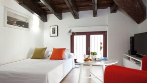 Une chambre d’hôtel avec un lit, une petite table avec une lampe, une télévision et un fauteuil rouge.