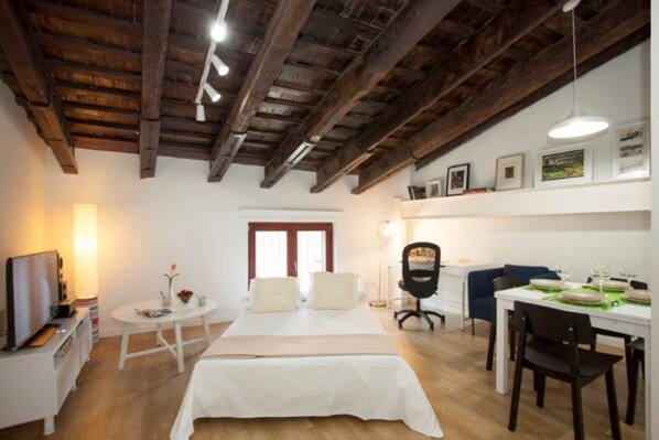 A bedroom with a bed, bedside table, lamp, and a desk with chairs.