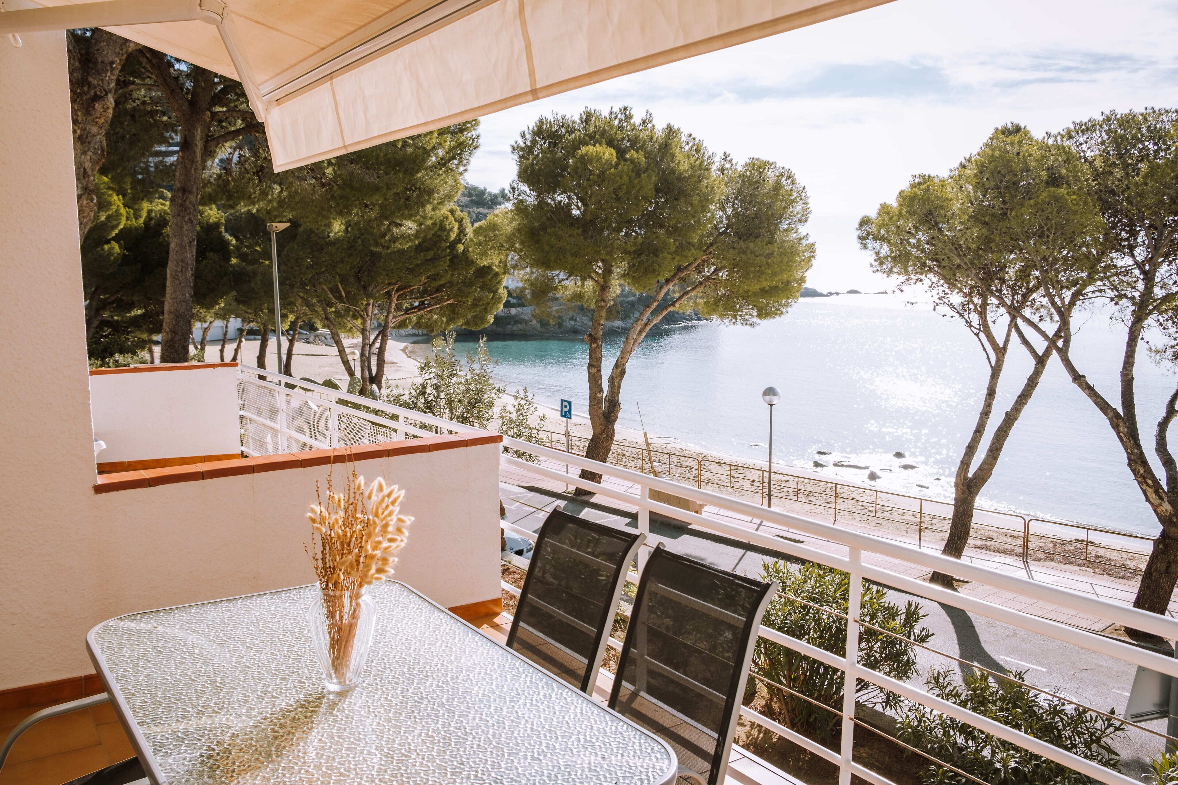 A balcony with a table and chairs, overlooking a beach and the sea.